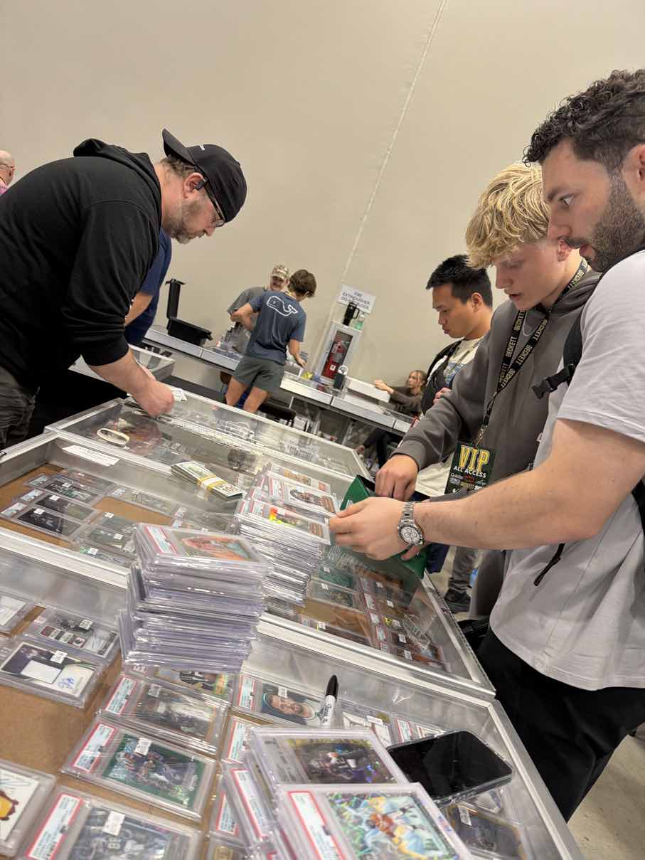 Mikey and the boys leaning over a glass showcase packed with graded cards on trade night